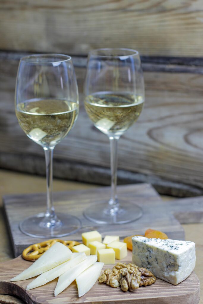 Twee glazen Sancerre wijn met kaasplankje met blauwe kaas, noten en snacks op rustieke ondergrond